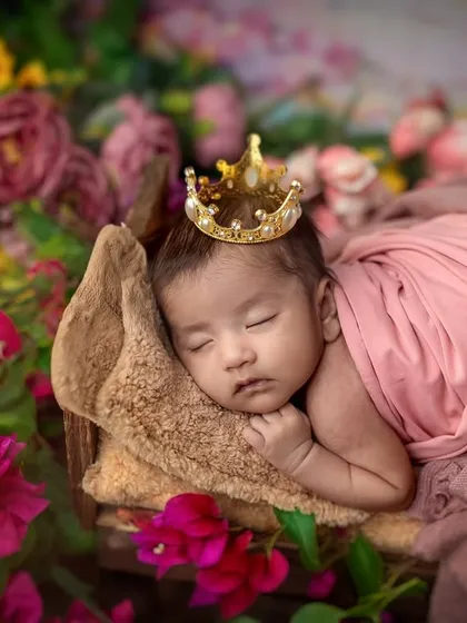 A tiny princess dreaming amongst the flowers. This newborn portrait showcases my gentle approach, using soft wraps, a delicate crown, and a bed of flowers to create a safe and beautiful setting for your sleeping baby.