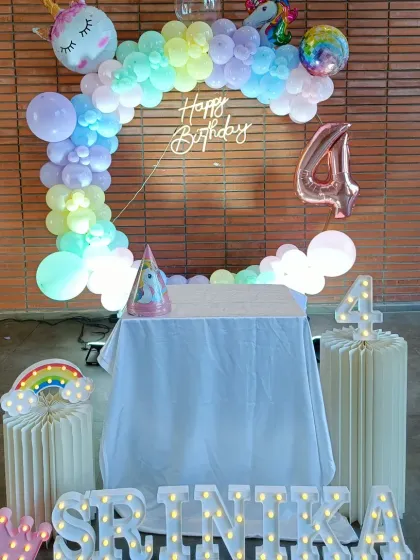 A whimsical unicorn-themed setup for Srinika's 4th birthday, featuring a pastel rainbow balloon ring and marquee letters.
