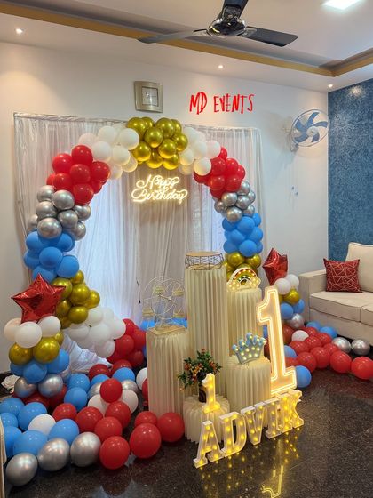 A centered shot of the first birthday balloon arch, highlighting the 'Happy Birthday' neon sign and the arrangement of pedestals with a light-up crown and number '1'.