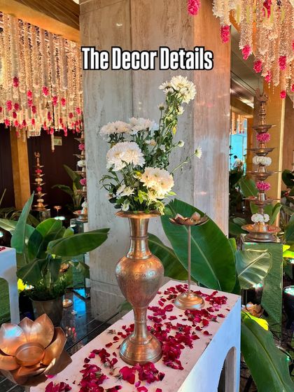 A beautiful detail shot of a brass vase with white flowers, set against a backdrop of hanging floral strings, capturing the essence of traditional elegance.