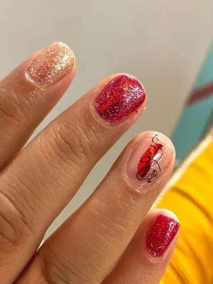 A cute and simple design featuring red glitter polish and a minimalist face sticker art accent.