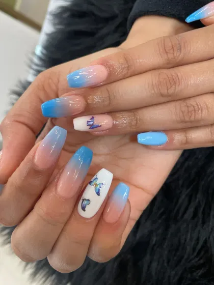 A beautiful blue ombré on long coffin nails, with white accent nails featuring delicate butterfly designs.