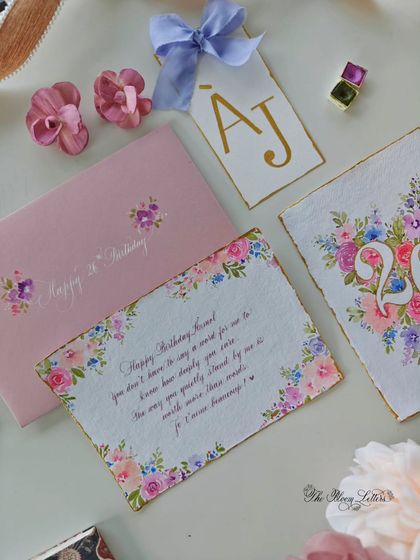 A flat lay of the complete birthday suite, including the hand-painted letter, a floral monogram card, a personalized tag, and a matching envelope.