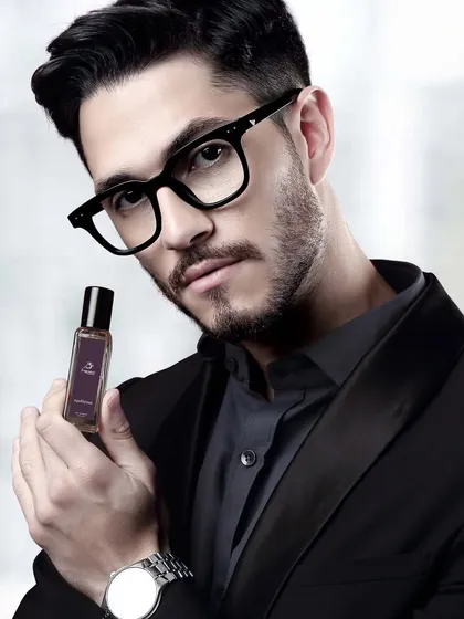 A sophisticated shot of a male model holding a perfume bottle. The dark, elegant styling makes this ideal for a luxury fragrance brand's advertising.