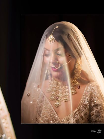 A soft and ethereal bridal portrait. The bride looks down, her face partially covered by her delicate veil, creating a dreamy and romantic image.