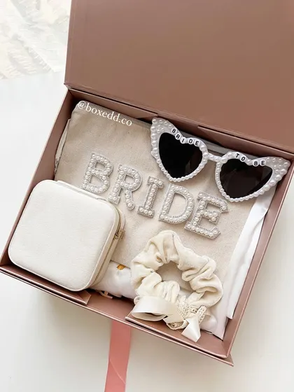 A celebratory gift box for the bride-to-be, featuring a 'BRIDE' pouch, heart-shaped sunglasses, a jewelry case, and a scrunchie.