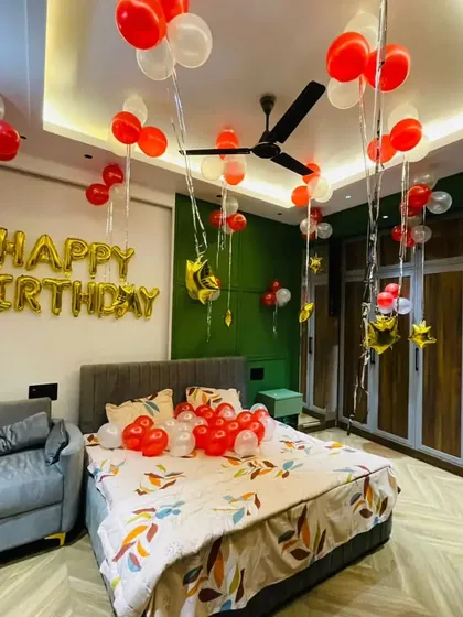 A simple and classic birthday room decoration with red and white balloons on the bed and ceiling, complemented by large gold foil 'Happy Birthday' letters on the wall.