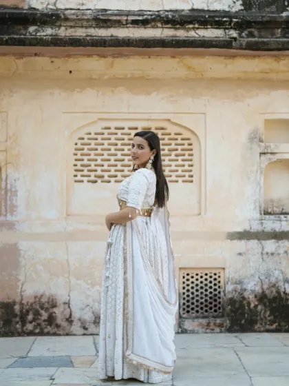 A stunning portrait of the bride in an elegant white lehenga. The soft, natural light and the textured palace wall create a serene and graceful image, perfect for a royal pre-wedding album.