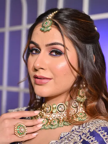 A full sangeet look with a royal blue lehenga and contrasting green jewelry. The makeup features a bold eye to match the drama of the outfit, creating a stunning and memorable appearance.