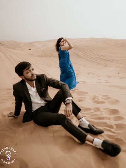 An artistic shot with the groom in the foreground, creating a sense of depth and perspective in the desert.
