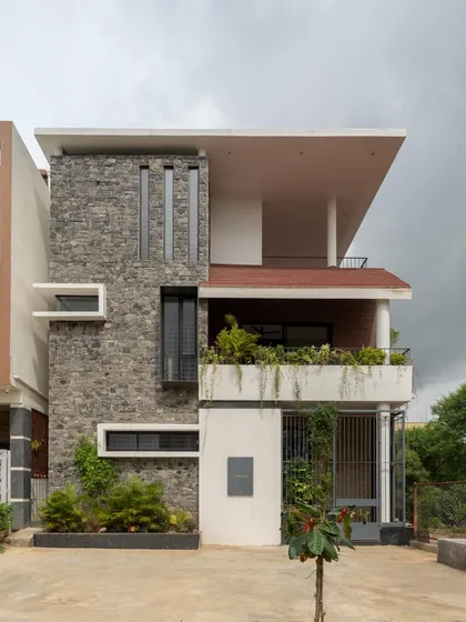 The compact exterior of the 'Bodhisatwa' home uses a mix of stone cladding, white plaster, and strategically placed windows to create an elegant and understated facade.