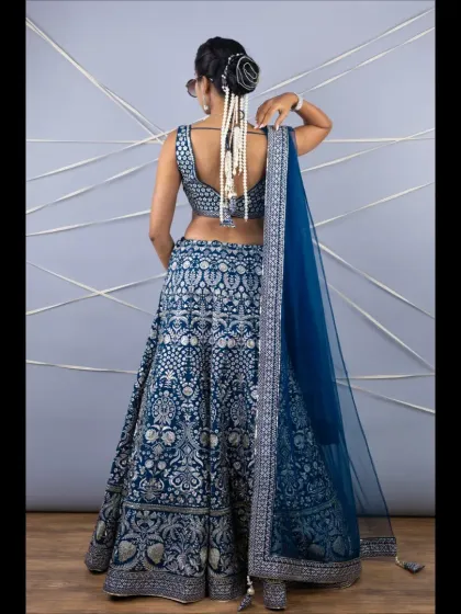 The back view of the navy blue lehenga, highlighting the deep back of the blouse and a stylish pearl hair accessory.