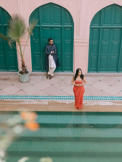 A wide shot of a couple standing by the pool at a palace, with the beautiful architecture in the background.