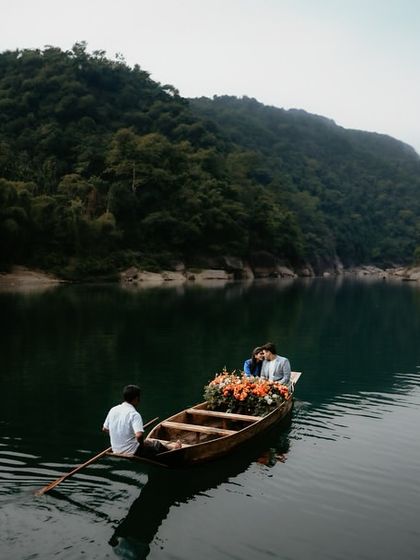 A serene and romantic scene of a couple in a flower-adorned boat on the tranquil waters of a Meghalaya lake. This wide shot captures the peace and intimacy of a private, nature-filled escape.