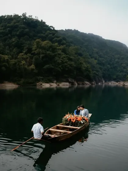 A serene and romantic scene of a couple in a flower-adorned boat on the tranquil waters of a Meghalaya lake. This wide shot captures the peace and intimacy of a private, nature-filled escape.