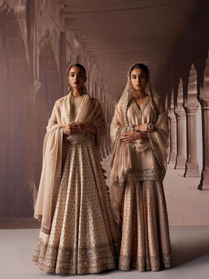 Two models styled in elegant, muted gold and beige outfits for a lookbook. The coordinated styling shows how to create a sophisticated theme for a bridal party using shararas and lehengas.
