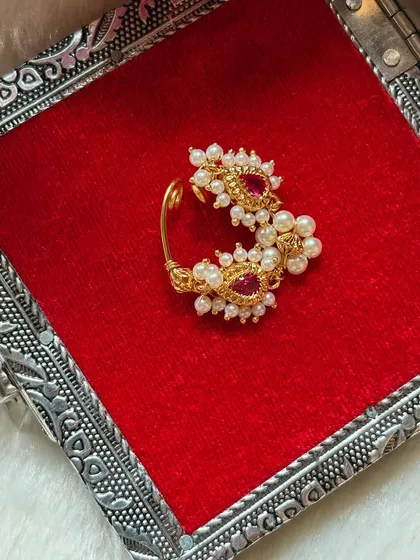 A beautiful clip-on Nath with red stones and pearls. This design is perfect for those who don't have a nose piercing but still want the traditional look.