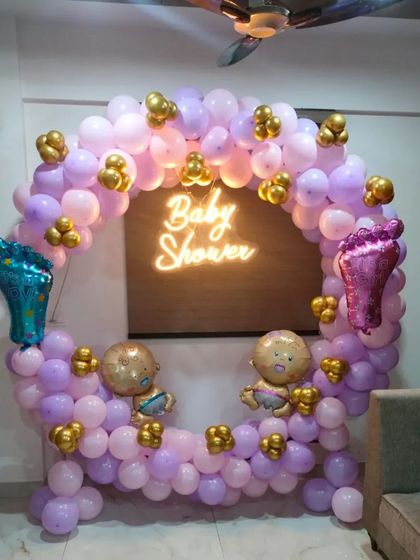 A full balloon ring in shades of purple and pink for a "Baby Shower." This vibrant setup includes a central neon sign and fun foil balloons shaped like baby feet and characters.