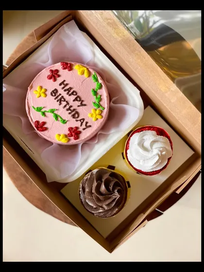 This colorful birthday combo includes a pink bento cake with floral decorations and two cupcakes, one chocolate and one vanilla. It's a perfect little party in a box.