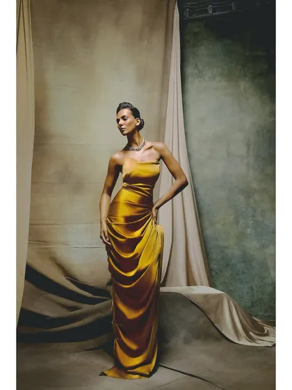 A stunning golden-yellow gown from the Ambika Lal campaign. The styling is pure classic glamour, with the draped satin catching the light beautifully against a muted, textured backdrop.