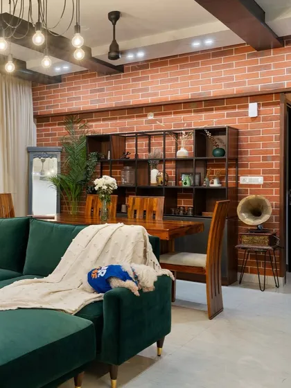 We love creating spaces with character. This industrial-chic living room features an exposed brick wall, a rich emerald green sofa, and warm wooden furniture. It’s a perfect example of how we mix textures and bold colors to create a home that is both sophisticated and inviting.