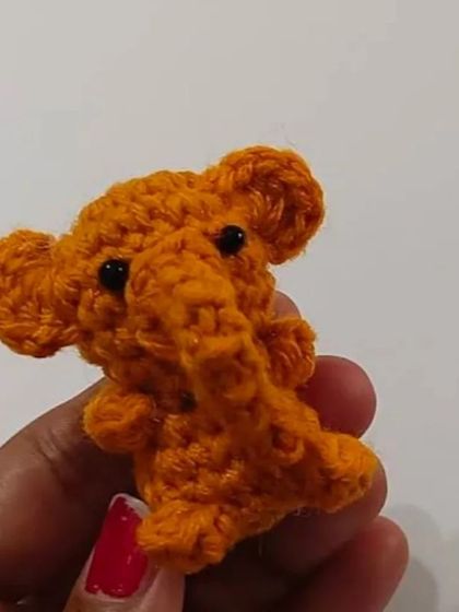 A tiny, bright orange crochet elephant. This miniature amigurumi is intricately made and can be ordered as a small toy or attached to a keychain.