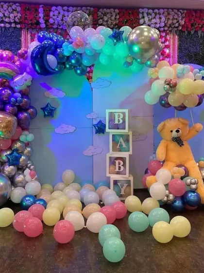 A whimsical 'BABY' themed decoration with a large teddy bear, 'BABY' boxes, and a rainbow-lit balloon arrangement.