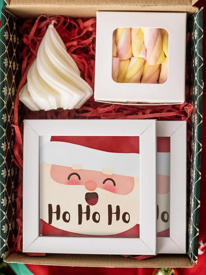 Spread the "Ho Ho Ho" cheer with this cute Christmas hamper. It contains a Santa-themed frame, a tree-shaped candle, and a box of fluffy marshmallows, perfect for a Secret Santa gift.