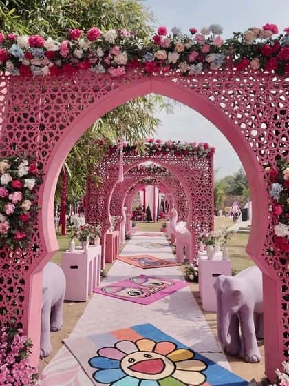 A vibrant Mehendi entrance in Jaipur, featuring hot pink jaali-work arches and a custom aisle runner with quirky, modern art designs. This setup perfectly blends traditional Rajasthani architecture with a playful, contemporary twist.