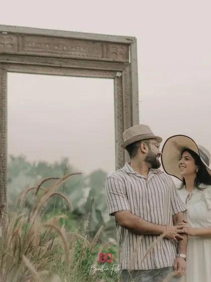 A creative pre-wedding shot using a large, empty frame in a field of tall grass. This setup adds an artistic and surreal touch to the couple's portraits.