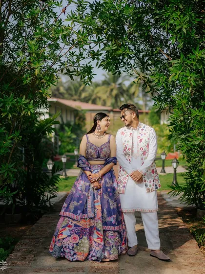 A full-length portrait of a couple in their stunning traditional outfits, framed by a natural arch of greenery at a Goa resort.