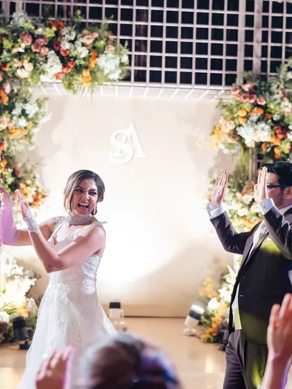 The dance floor is alive with energy. The couple and their guests celebrate in front of a stage framed by beautiful, lush floral arches.