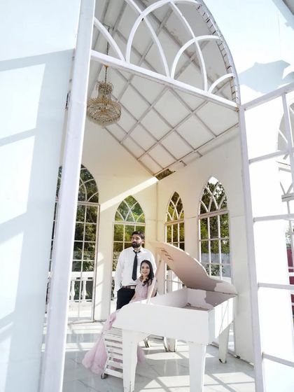 A wide-angle shot of the couple with the white piano, showing the beautiful architecture of the location.