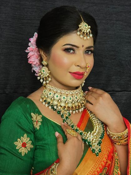 An elegant Maharashtrian look featuring a green and red Paithani saree. The makeup is classic, with defined eyes, a red lip, and a subtle bindi.