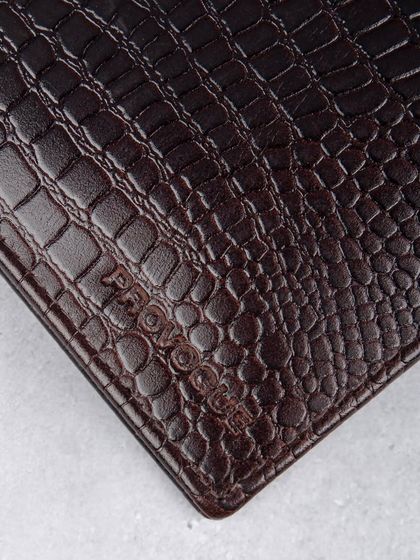 A macro shot of the embossed logo and texture on the dark brown crocodile wallet.