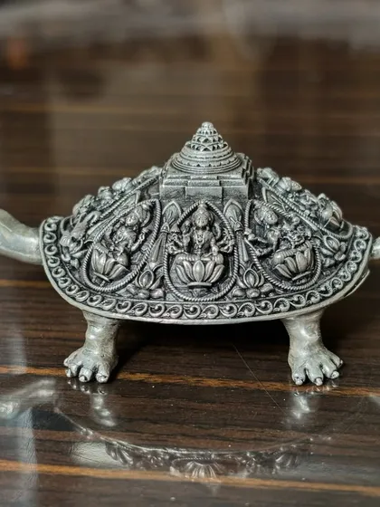 A side view of the lucky silver tortoise, featuring a temple-like structure on its back. The shell is intricately carved with figures of deities, making it a perfect Vastu or Feng Shui gift.