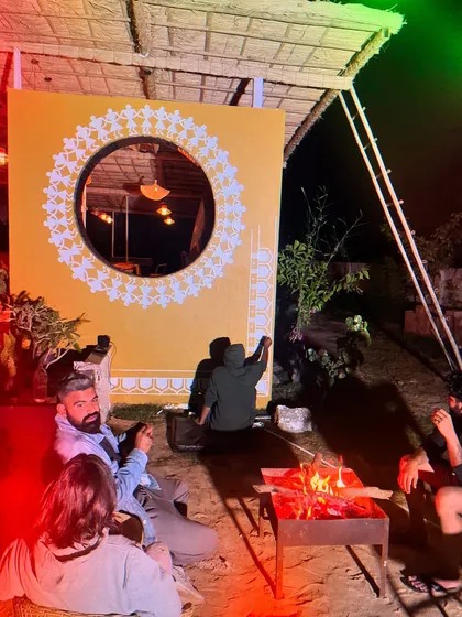 Painting the Warli art by the fire. This photo captures the cozy, creative vibe of working on-site at unique locations.
