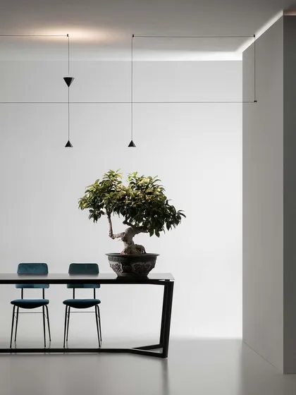 The Filomena system by Karman is the essence of minimalism. A simple black cone unfolds into a versatile system of suspensions, seen here creating a delicate graphic composition over a dining table.