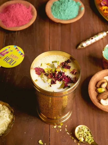A glass of refreshing Thandai, styled with all the elements of Holi: vibrant colors, nuts, and flower petals. This image captures the spirit of the festival.