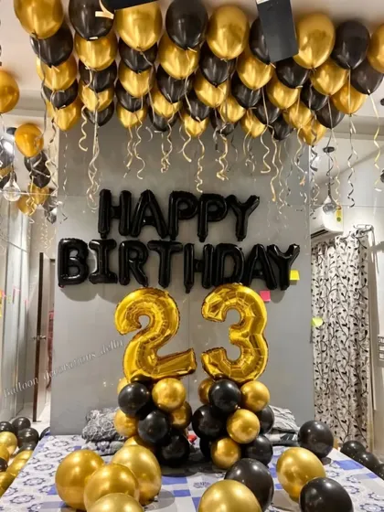 A bold black and gold theme for a 23rd birthday room surprise, with ceiling balloons and number balloon pillars.
