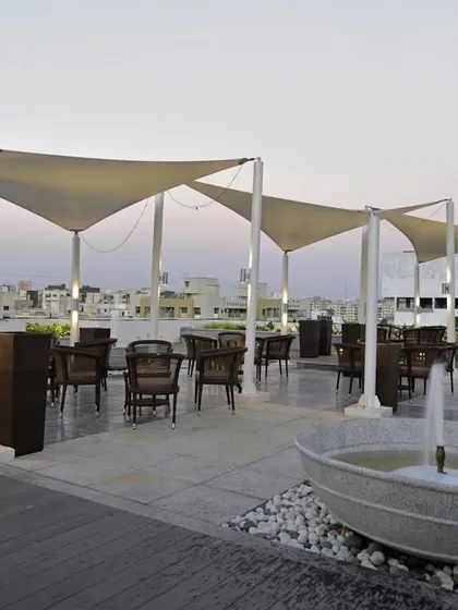 A rooftop coffee lounge with tensile fabric canopies for shade. The space includes comfortable seating and a small water feature, creating an urban oasis.