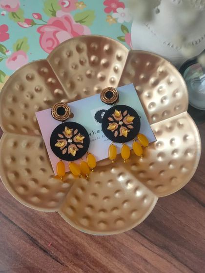 A pair of black fabric earrings with yellow floral embroidery and matching bead drops. The contrast of colors makes these a striking accessory for any occasion.