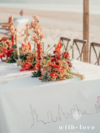A long table at the beach event, with a runner of tropical flowers and red glass vases.
