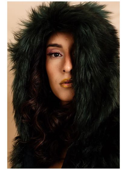 A beauty-focused creative shoot exploring texture and color. The combination of a faux fur hood, shimmering pink eyeshadow, and a bold metallic gold lip creates a striking and high-fashion portrait.