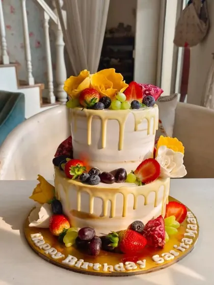 A fresh and vibrant two-tier fruit drip cake, adorned with strawberries, blueberries, grapes, and yellow sugar flowers.