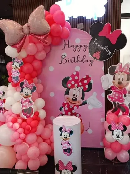 A classic Minnie Mouse theme for a birthday party. This decoration features a pink and red balloon arch, a Minnie Mouse backdrop, and character cutouts.