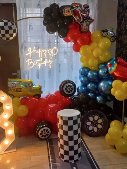 A complete Hot Wheels birthday setup with a ring arch, marquee number '3', and a custom checkered pedestal. The neon 'Happy Birthday' sign adds a cool glow.
