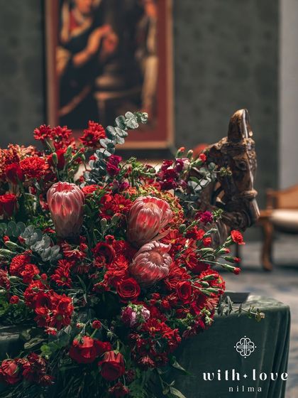 A beautiful floral arrangement in deep reds, with a wooden horse sculpture adding a touch of rustic elegance. The composition is rich in texture and color.