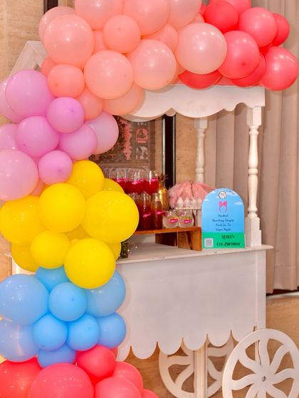 A colorful drink and snack cart for a Peppaland party. The cart is decorated with a vibrant balloon garland, tying it into the overall bright and cheerful theme of the event.