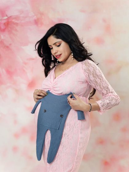 An expecting mother holds a little blue outfit against her baby bump. This is a sweet and simple way to announce you are having a boy.